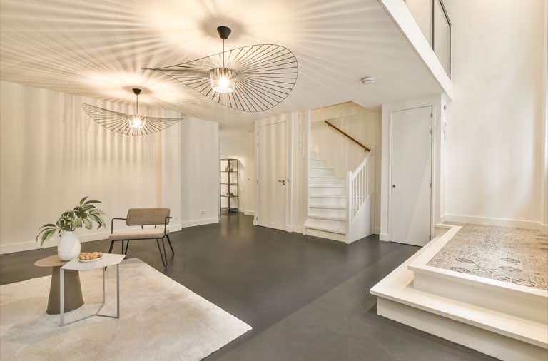 Salón moderno con muebles minimalistas, suelo negro, paredes blancas, lámparas de techo únicas, una escalera y una pequeña zona elevada de azulejos que muestra una reforma de lujo.